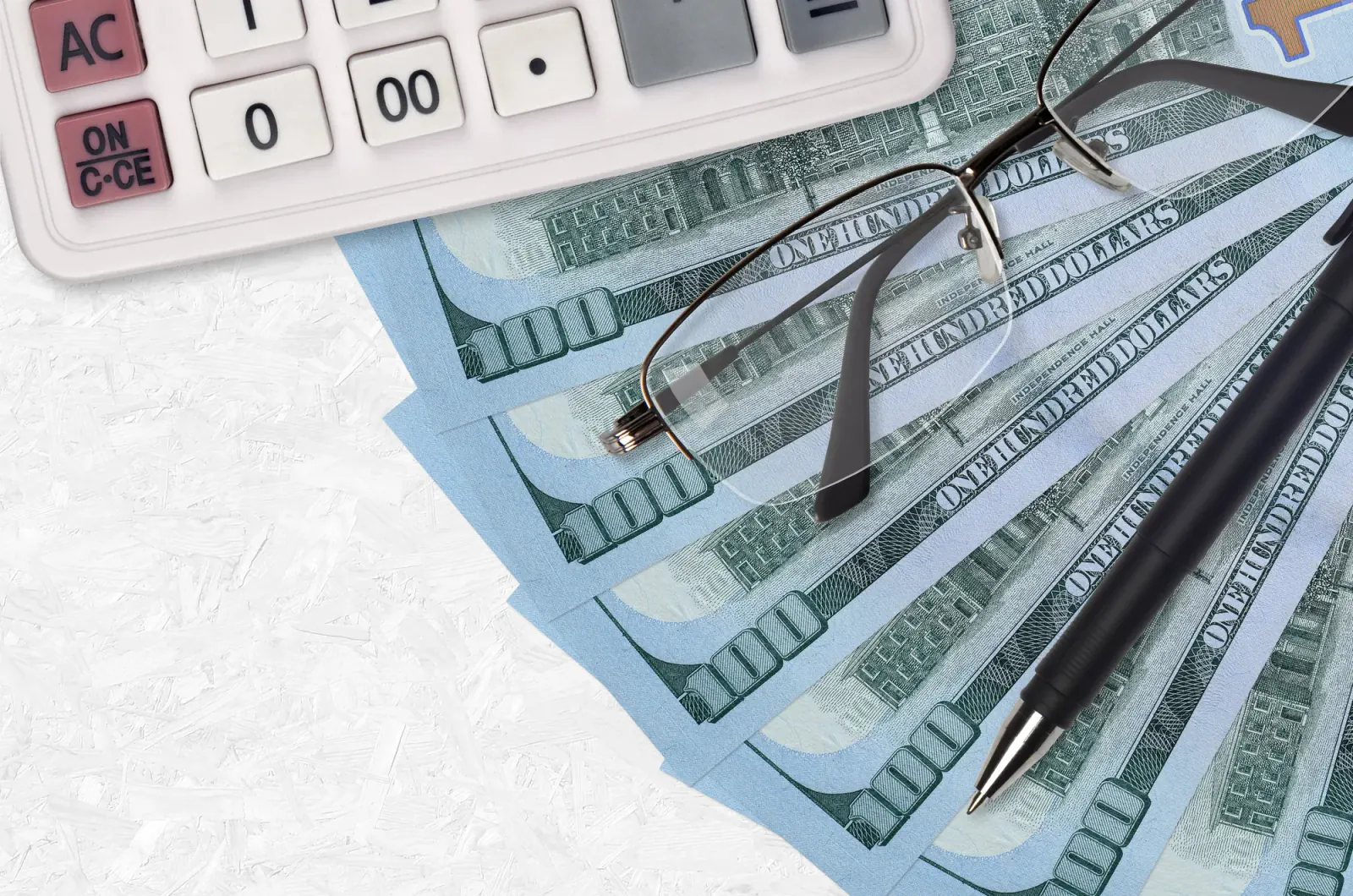 Calculator, US currency, eyeglasses, and pen arranged for tax planning